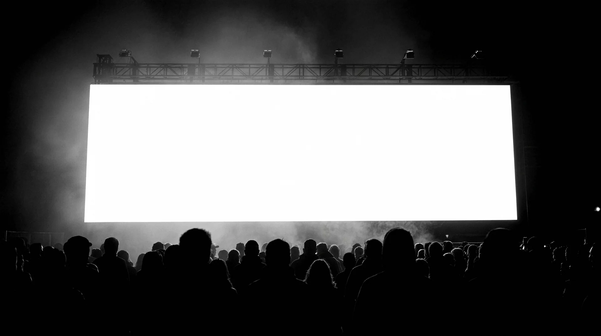 Una multitud en silueta, de espaldas, mirando un cartel publicitario gigante iluminado.